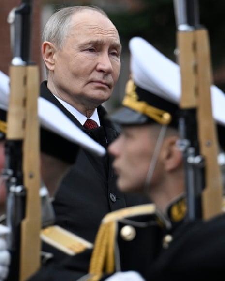 Vladimir Putin stands among military personnel holding rifles with white caps