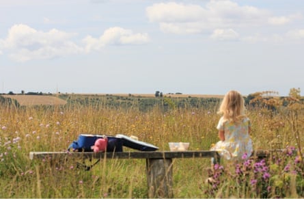 A young girl sits on a bench looking over a wildflower meadow