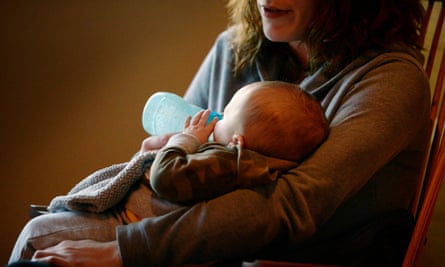 A white woman, her face out of the frame, sits in a rocking chair feeding a newborn from a bottle.