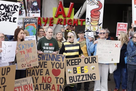 A crowd of people holding cardboard signs with messages including Save Our Scotland, Keep our Bees Buzzing, Say No To the AI Centre in Larbert, and Stop the Datacentres.