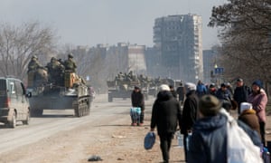 Service members of pro-Russian troops drive armoured vehicles past local residents in the port city of Mariupol.