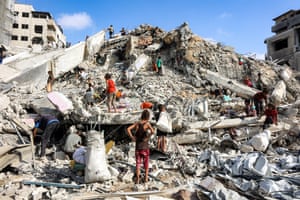 People standing on huge pile of rubble, some of them carrying white sacks