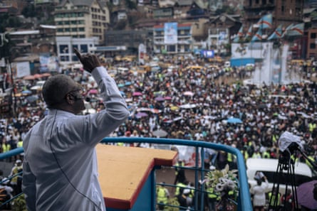 An African man gesticulates as he speaks before a very large crowd.