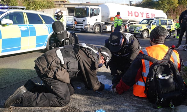 Police try to unglue a protester from the surface of the road in South Mimms