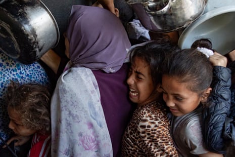 O povo palestino deslocado se reúne do lado de fora de uma cozinha de caridade em Gaza City para receber rações limitadas de alimentos.