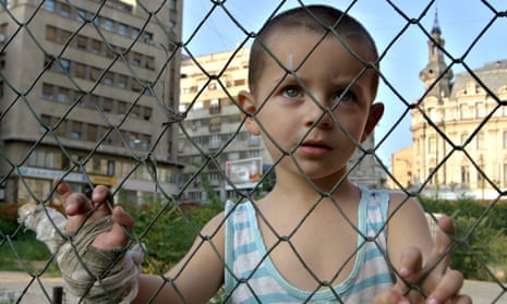 Romanian street child looks on through a fence