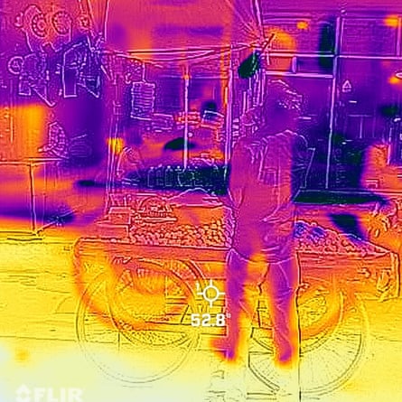 A thermal image shows a person standing at a street cart. The top half of the image is purple and the lower half is yellow