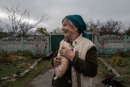 Vera Borisovna stands in front of her house in the recently liberated village of Snihurivka, holding a loaf of bread she received from humanitarian aid.