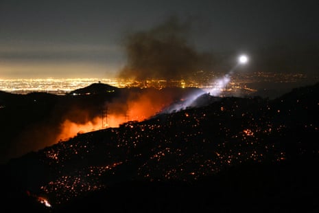The light of a firefighting helicopter illuminates a smouldering hillside