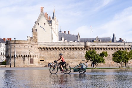 Cyclist with trailer pedals through water beside a medieval castle
