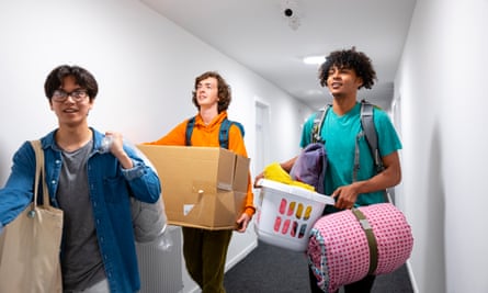 A medium close-up of three young male students and friends walking to their new rooms in their student accommodation. They are carrying bedding and washing baskets