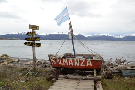 An old rowing boat painted with the words ‘Puerto Almanza’. An Argentinian flag flies above it and a rough wooden signpost stands beside it 