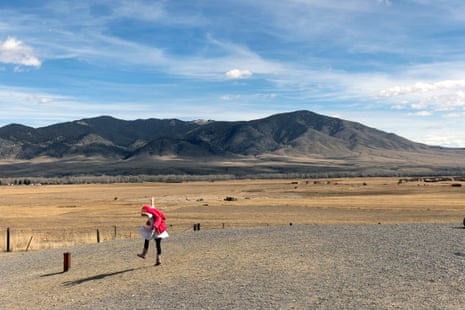 A girl wearing a pink sweater is shown leaping in the foreground, with mountains visible in the background.