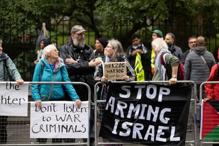 People hold up signs saying ‘stop arming Israel’ and ‘Don’t listen to war criminals’