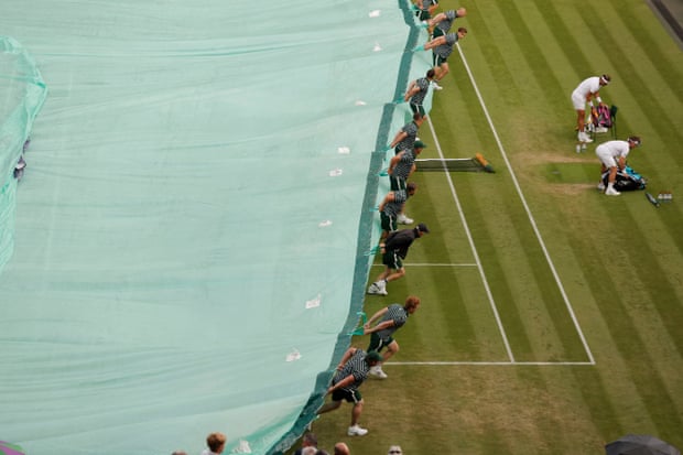 Rafael Nadal and Ricardas Berankis hurriedly pack up their bags as groundsmen rush to cover the court from a shower of rain on Centre Court.