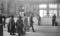 A woman directs two women in shawls across Keleti station in this black and white image, Budapest, Station, 1975 by Bertien van Manen.