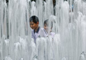 Two children in T-shirts smile, surrounded by fountains of water