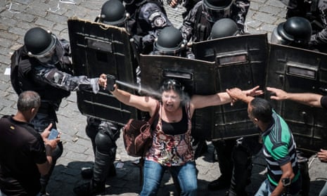 A heavily armed riot policeman squirts pepper spray into a woman protester's face