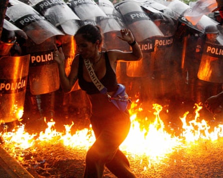 A protester runs in front of riot police, with flames at their feet