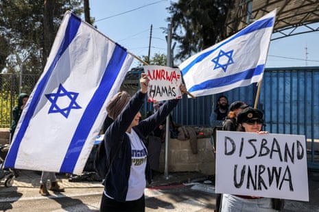 An Israeli protester holds a flag and a sign while standing with others outside an Unrwa office in Jerusalem.