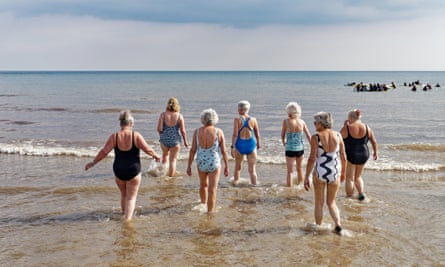 A group of women are ankle deep in the sea as they wade in to go for a swim