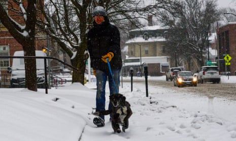 Man walks dog down snowy sidewalk