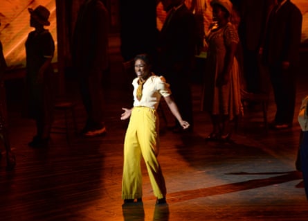 Erivo mid-song on stage, wearing high-waisted yellow trousers.