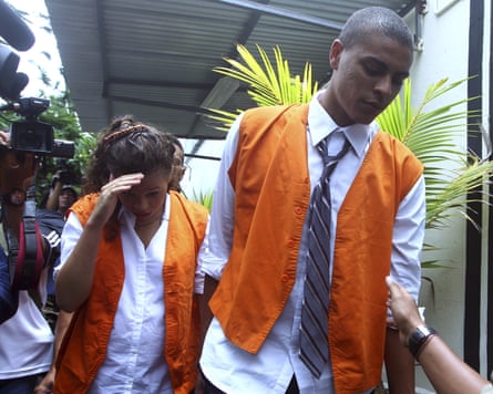 Schaefer and Mack, both wearing white shirts and casual orange waistcoats, walk past a crowd of photographers