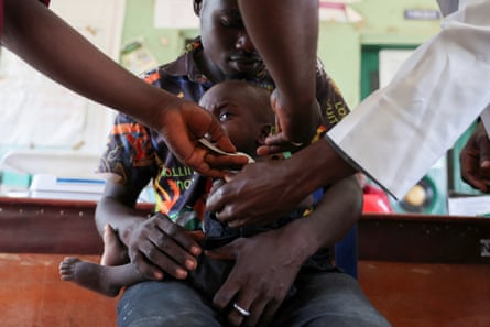 A young man holds a small child on his lap as the hands of healthcare workers can be seen attending to him