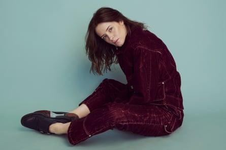 Claire Foy sitting on the ground wearing a dark red velvet jacket and trousers by Stella McCartney and Erdem brogues