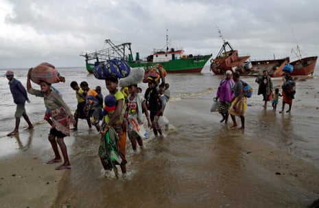 Families arrive on a beach in Mozambique carrying belongings wrapped in fabric bundles on their heads
