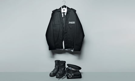 Police uniform on a hanger above police boots and hat, against grey background