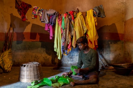 Chhotray Hembram sorts leaves, sitting on the floor of a bare room hung with washing