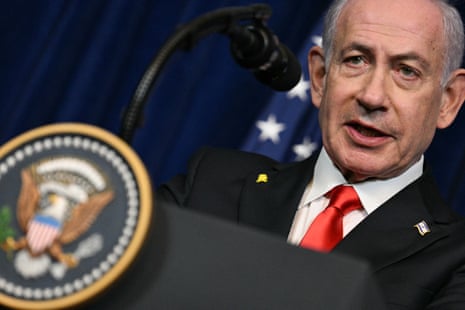 A man in a suit and red tie speaks at a podium