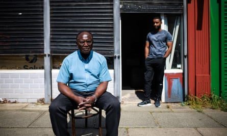 Nelson Shardey sitting on a chair outside a shop unit with the shutters down. Jacob Shardey leans on a wall in the background.