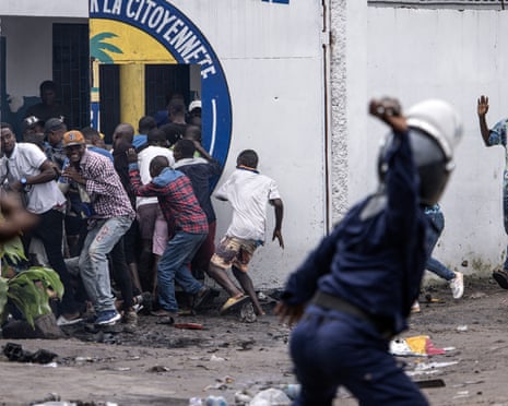 A police officer throws a stone as people into a building for cover