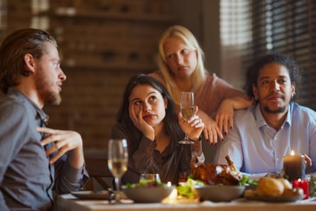 Four people around a table, one holding court while others look bored