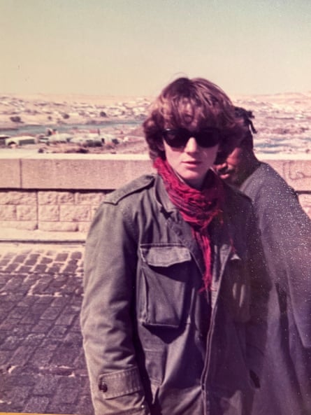 A young man wearing an ex-army jacket, sunglasses and a red scarf.