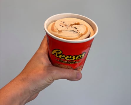 A hand holding a tub of peanut butter and milk chocolate ice-cream
