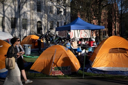 people walk by tents near a campus building. A sign says ‘divest’, in a color photo