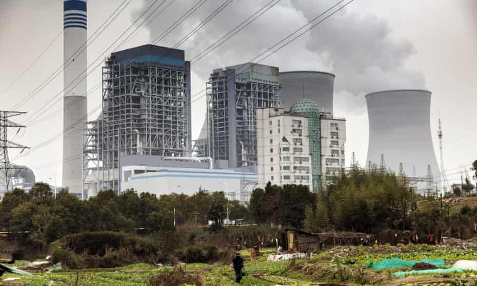 A man walks past vegetables growing in a field as emissions rise from cooling towers at a coal-fired power station in Tongling, Anhui province, China.