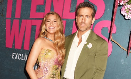 a blonde woman in a colourful strapless gown and a man in a khaki jacket pose on a red carpet