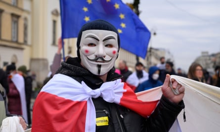 a man in a guy fawkes mask wearing a historical belarusian flag with an eu flag in the background