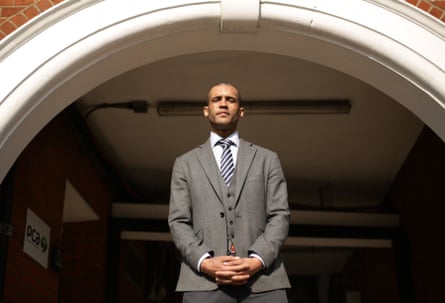 A man of colour in a grey suit standing under a white arch