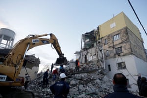 Emergency personnel using a digger beside a collapsed building