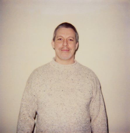 A polaroid shot of a man with cropped grey hair wearing a beige flecked jumper