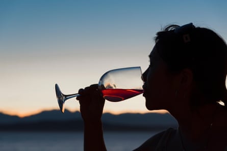 A silhouetted woman drinking a glass of red wine with the sunset in the background
