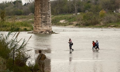 A Texas National Guardsman watches as a group of migrants wades across the Rio Grande.