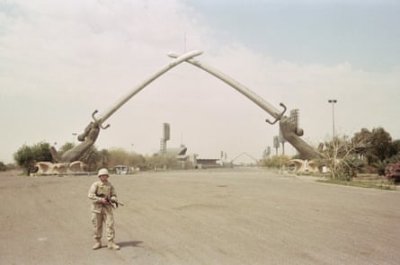 a soldier stands on a road in front of large sculpture of two hands carrying swords