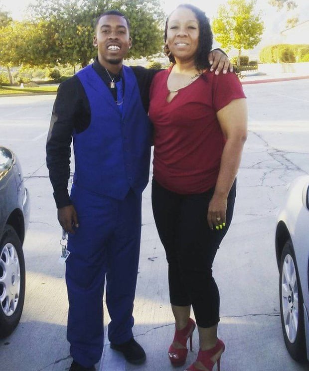 A man in a blue vest and black shirt is standing with his arm around a woman in a red blouse.